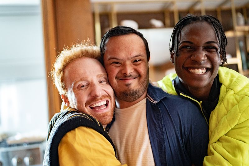 Three friends laugh together with their arms around each other.