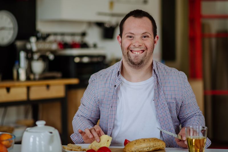 A smiling man eats breakfast at his kitchen table.