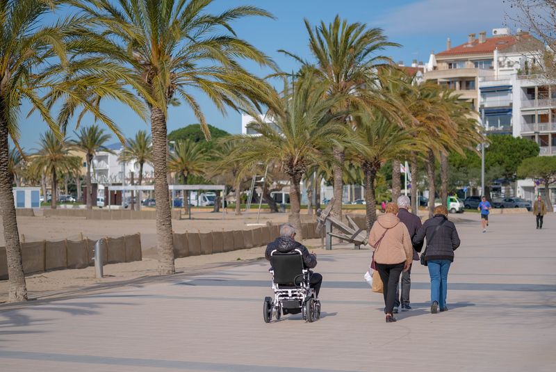 A man in a power wheelchair rolls along a seaside promenade with friends.