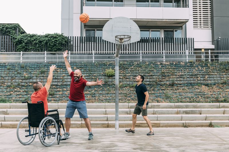 Friends play basketball together, one in a wheelchair.