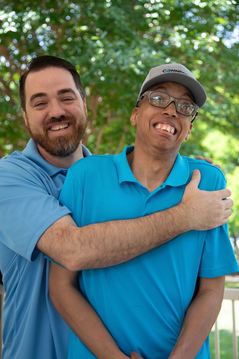 Two friends in matching blue shirts hug and smile.