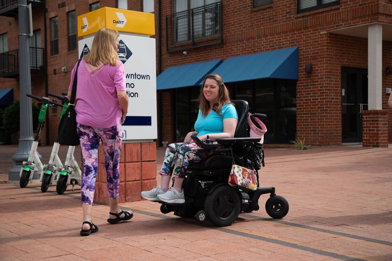 Two women, one in a power wheelchair, pass a downtown train station.